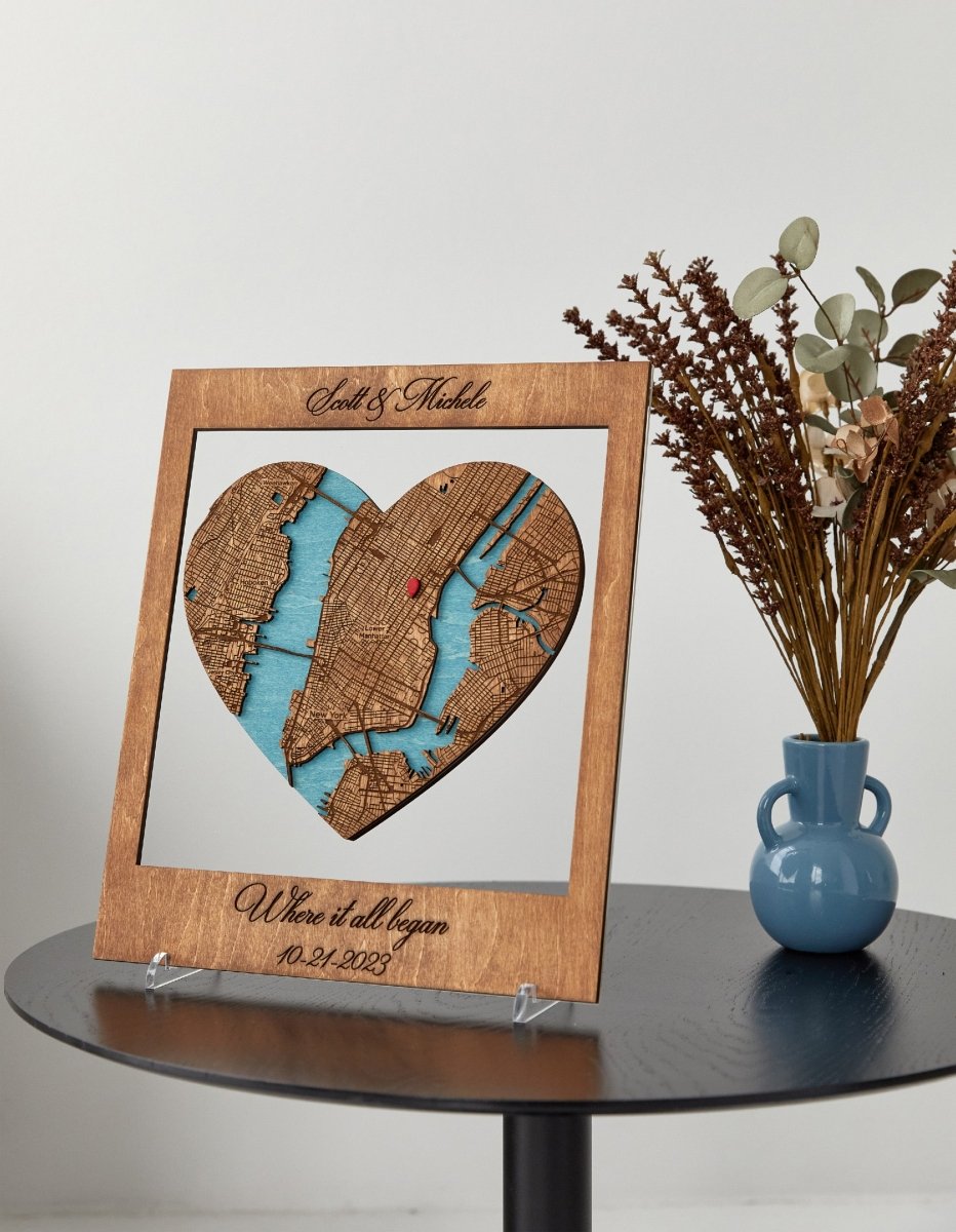 Heart-shaped wooden map with engraved text on a table with a vase and flowers.