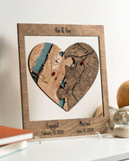 Customized heart-shaped map puzzle in a frame by a person against a wall, featuring two locations with dates for engagement and married