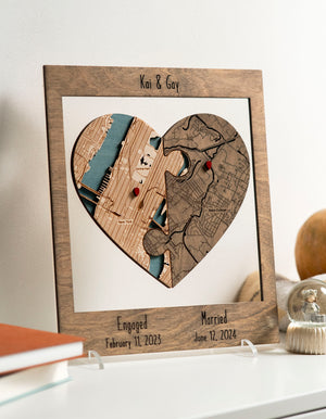 Customized heart-shaped map puzzle in a frame by a person against a wall, featuring two locations with dates for engagement and married