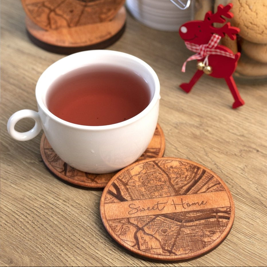White mug with tea on wooden coasters with 'Sweet Home' engraving, surrounded by cookies and a red reindeer figurine.