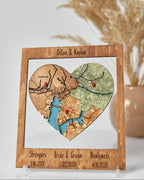 Heart-shaped map cutout with personalized text on a wooden frame, displayed against a neutral background.