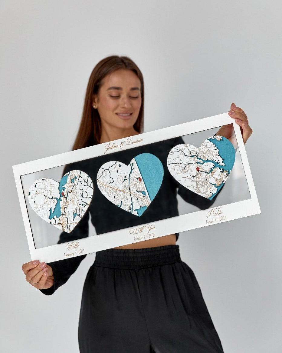 Person holding a framed map art piece with heart shapes on a gray background