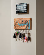 Key holder with keys attached to a wall, featuring a decorative wooden panel with a map design.