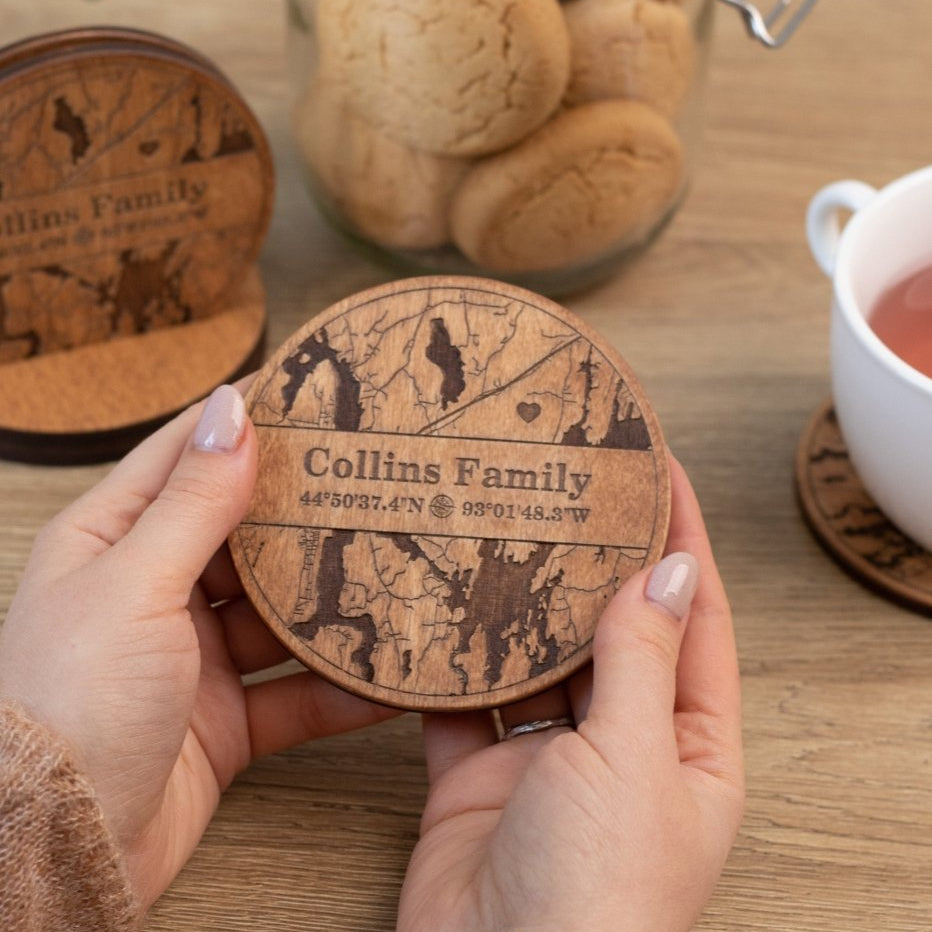 Person holding a wooden coaster with 'Collins Family' engraving on a table with cookies and tea.