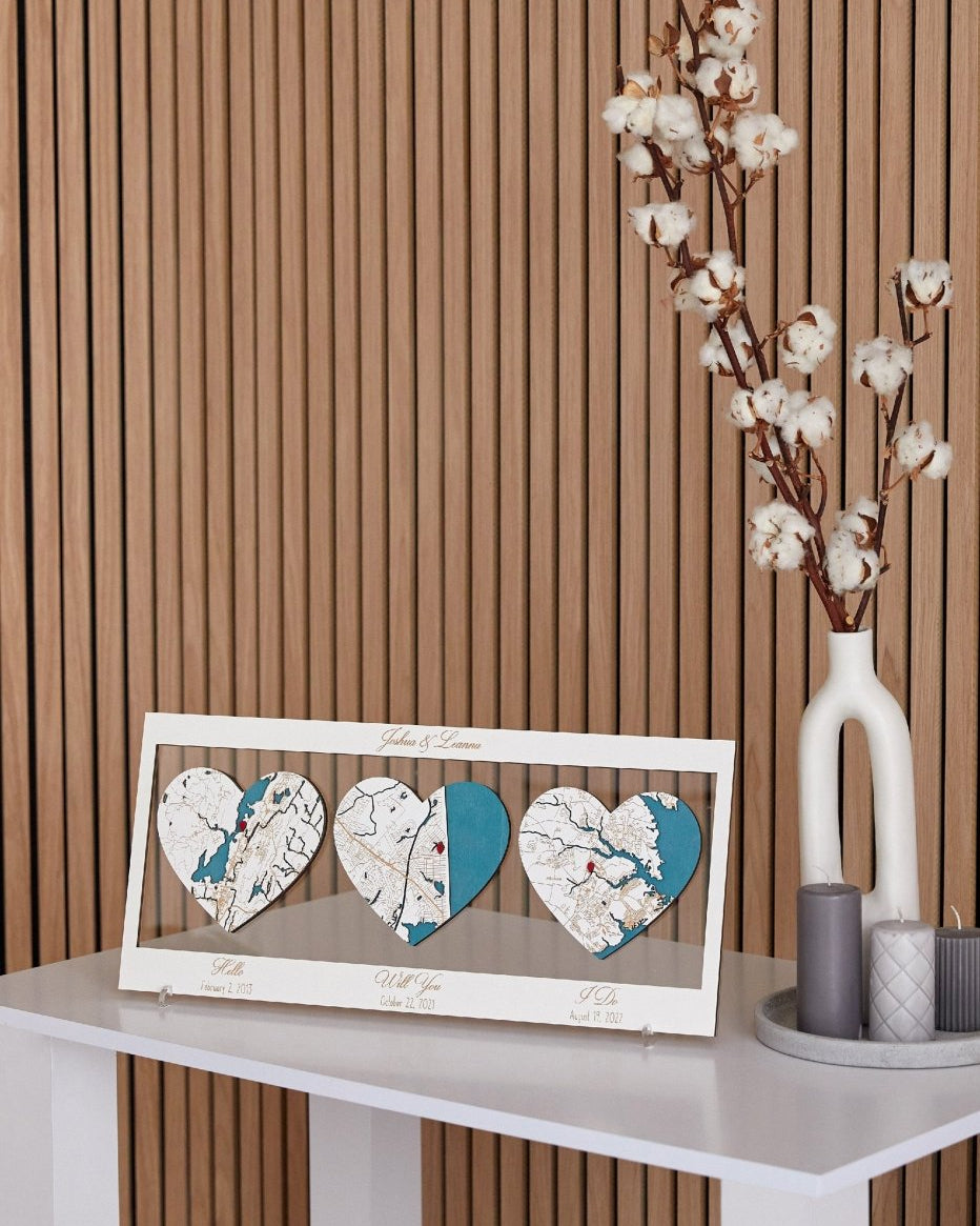Decorative heart-shaped map display on a table with a vase of cotton branches against a striped wall.