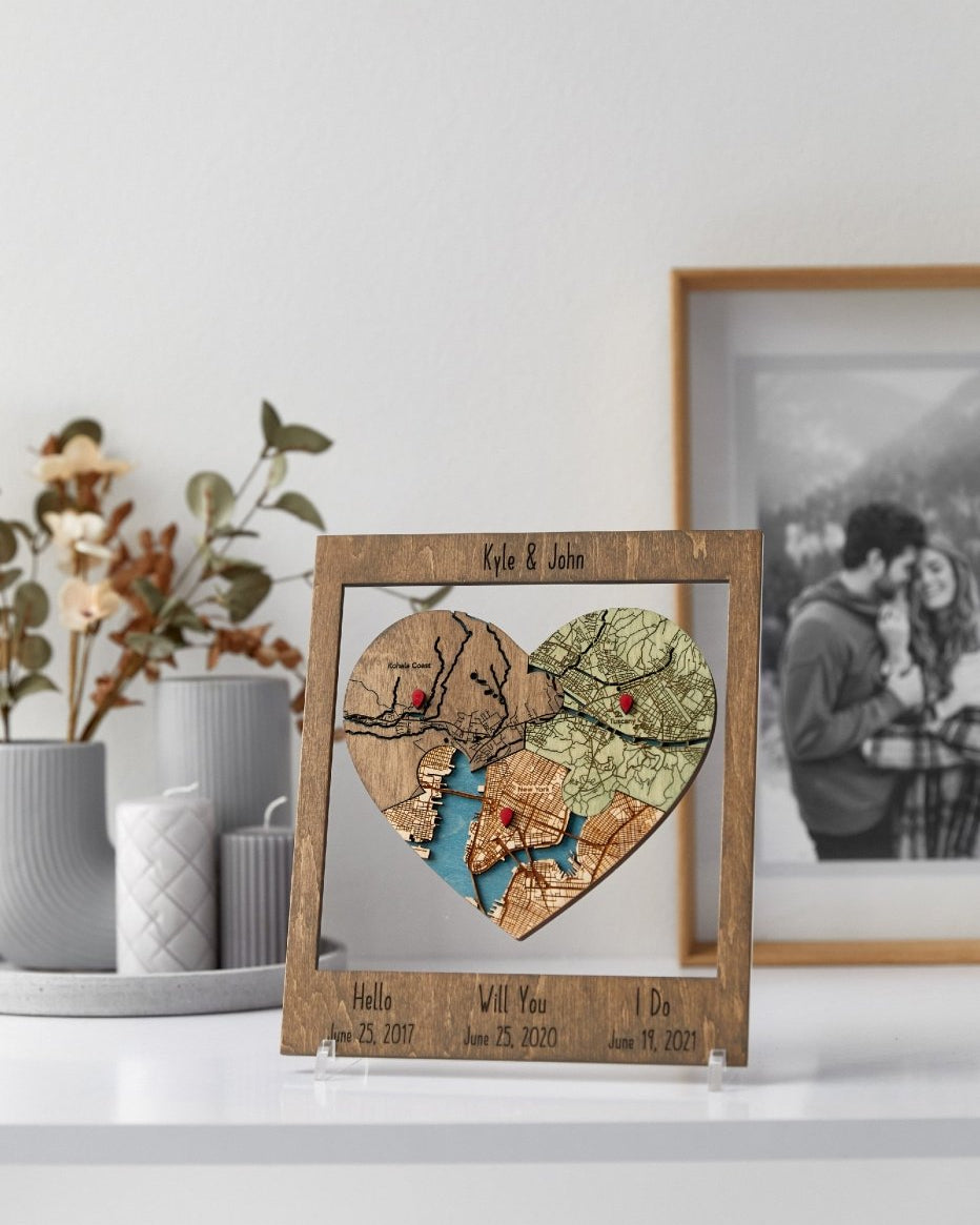 Heart-shaped map mosaic in a wooden frame on a white surface with decorative items in the background.