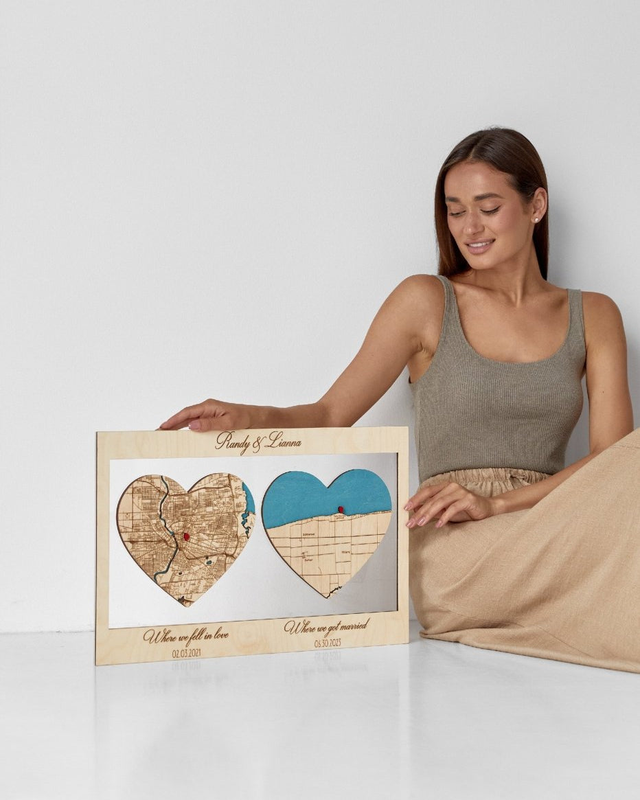 Woman holding a framed heart-shaped map of a couple's hometowns with a white background