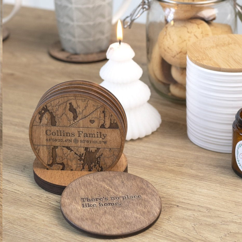 Wooden coasters with engraved designs on a wooden surface with a candle and cookies in the background.