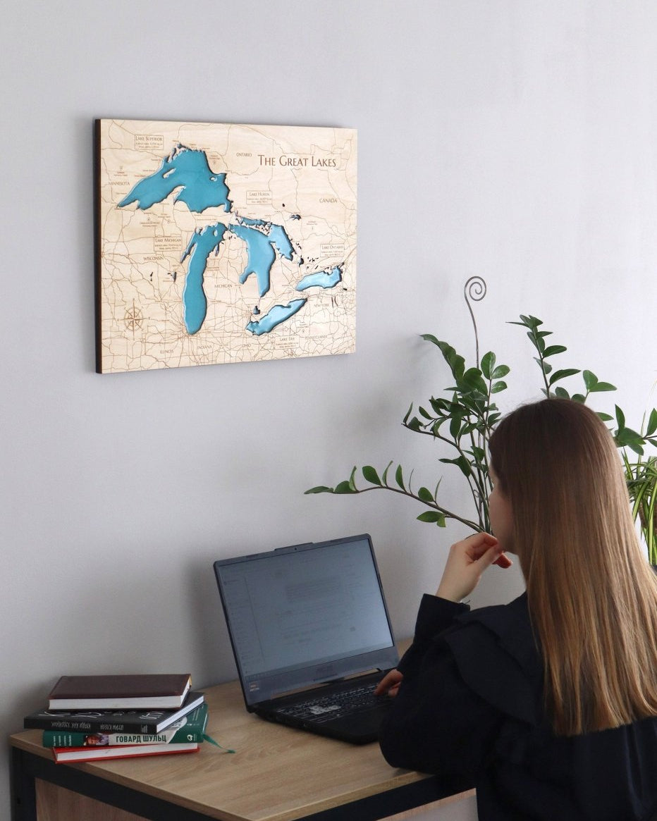 Person sitting at a desk with a laptop, looking at a wall-mounted map of The Great Lakes.