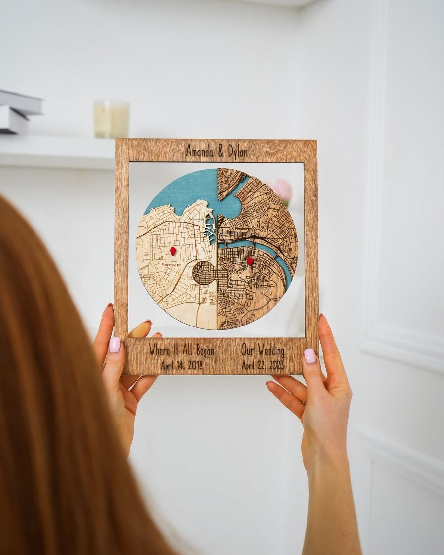 Person holding a wooden framed map with two locations marked, against a white background