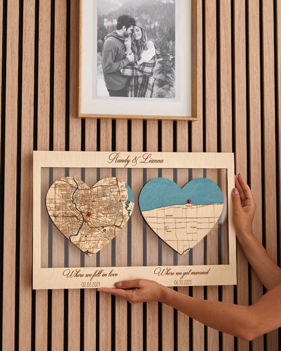 Heart-shaped map cutout with personalized text on a wooden frame, held by a person against a striped wall.