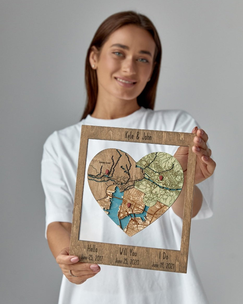 Woman holding a framed heart-shaped map collage with personalized text on a gray background