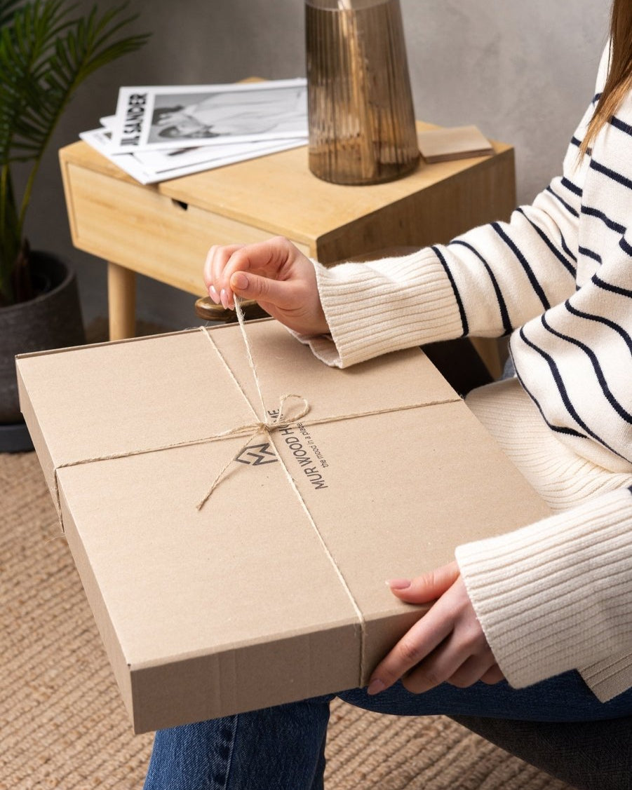 Person opening a brown gift box with a visible brand logo on a wooden table.