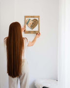 Person hanging a framed heart-shaped artwork on a white wall