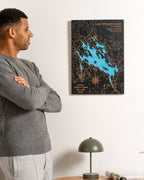 Man looking at a wall-mounted map of Lake Winnipesaukee in a room with a lamp and rolled-up map on a table.