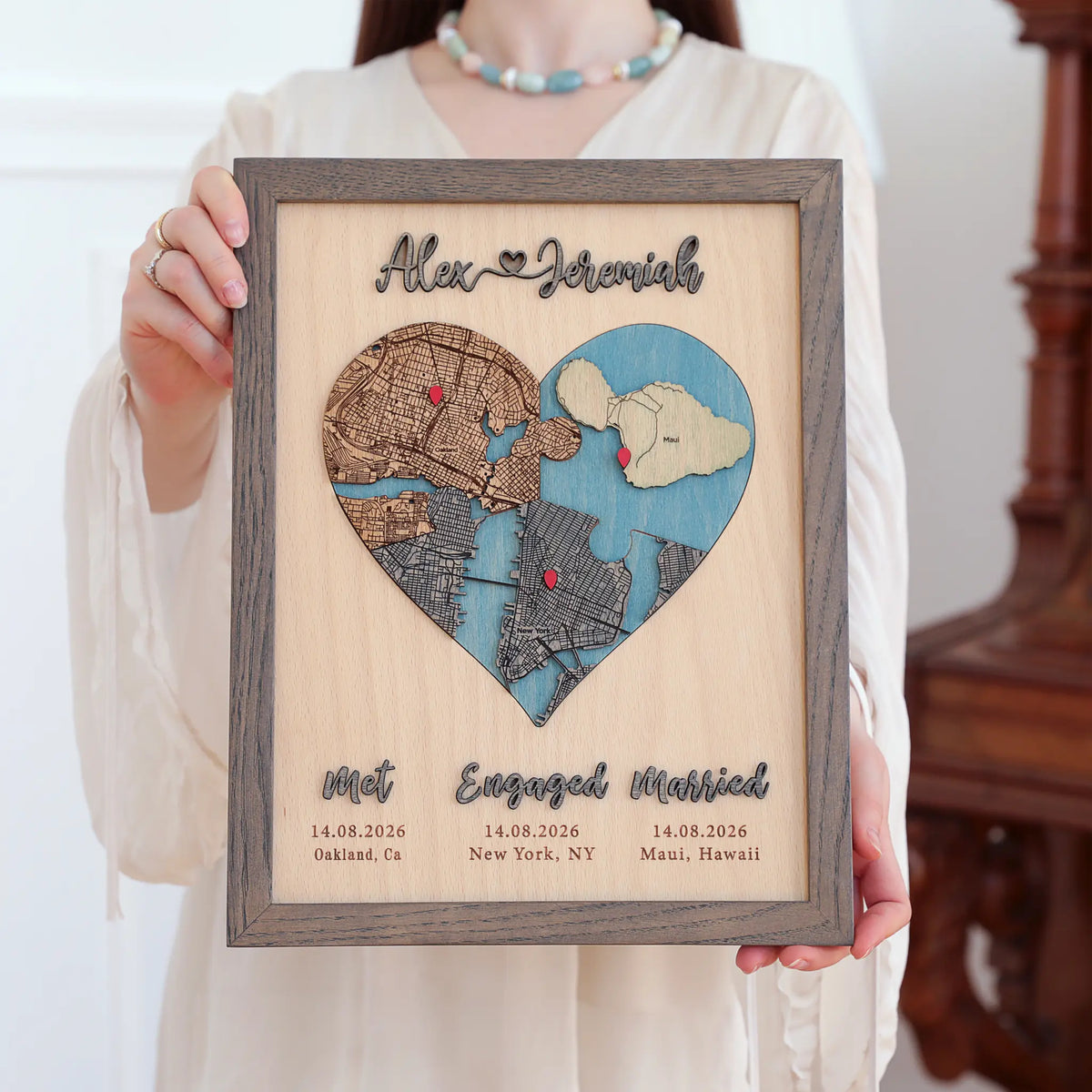 Woman holding a three-location wooden heart map in a Grey oak frame with Met, Engaged, Married labels.