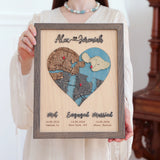Woman holding a three-location wooden heart map in a Grey oak frame with Met, Engaged, Married labels.