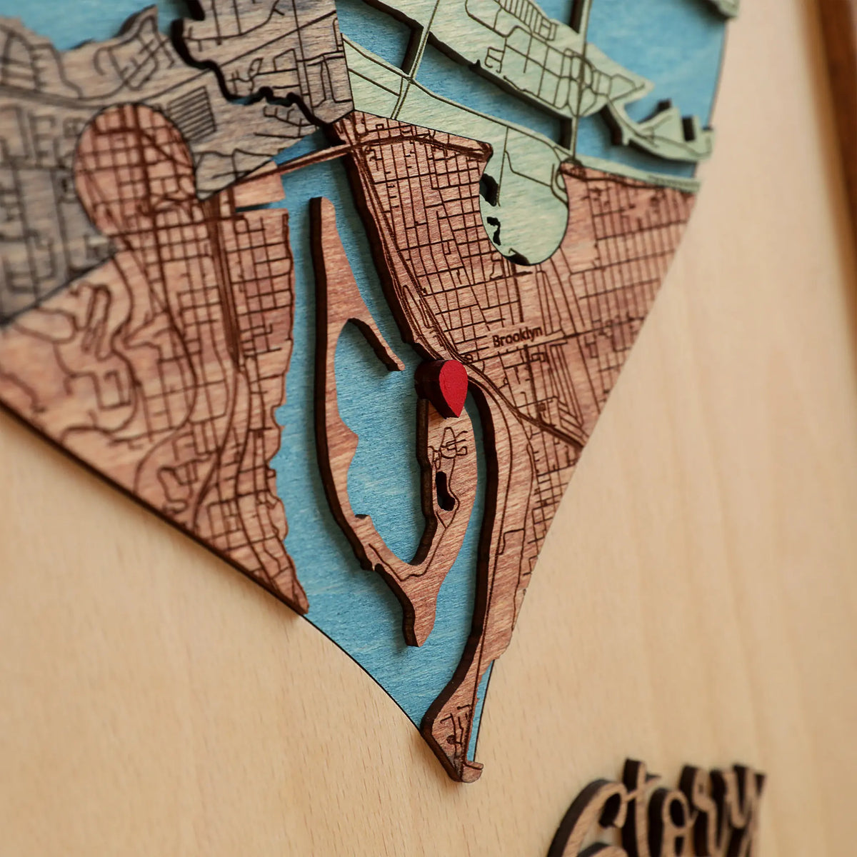 Close-up of layered wooden map sections, blue waterways and a red location marker in a three-part heart map.