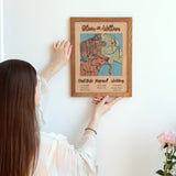 Woman positioning a framed Classic Square three-location wooden map on a wall.