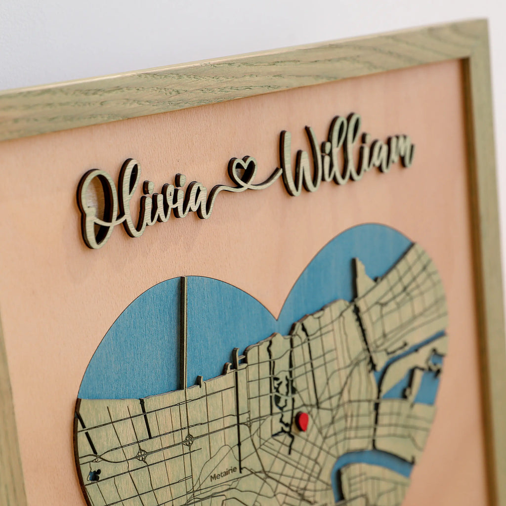 Close-up of raised laser-cut Olivia and William names above a heart-shaped New Orleans map, showing layered wood details and sage oak frame.