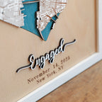 Close-up of raised laser-cut Engaged lettering with custom date and New York location on a personalized wooden anniversary map in white frame.