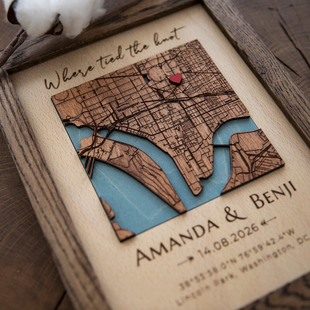 Close-up of custom wooden location map with red heart pin, engraved streets, blue water, and wedding coordinates