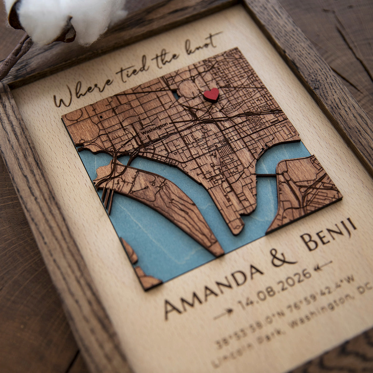 Close-up of custom wooden location map with red heart pin, engraved streets, blue water, and wedding coordinates