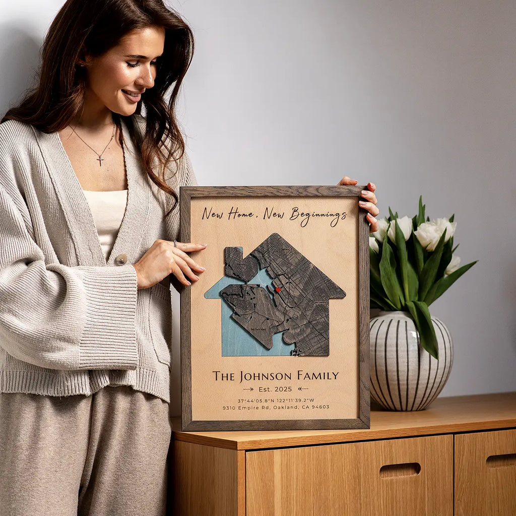 Woman displaying house-shaped personalized wood map frame with “New Home, New Beginnings,” family name, and established year.