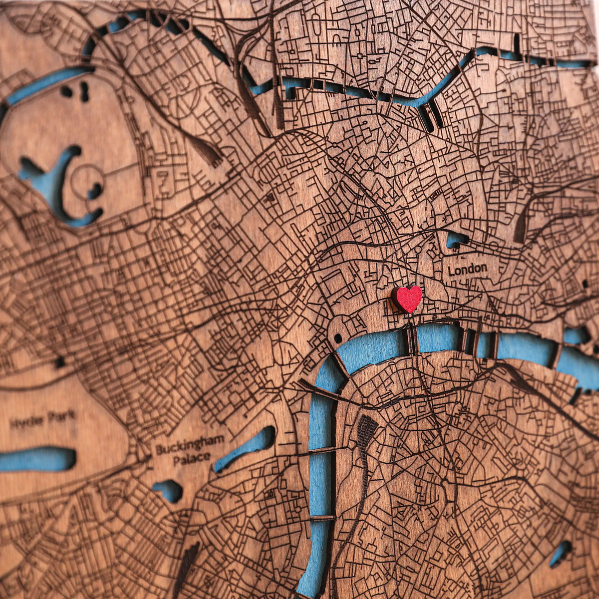 Close-up of detailed laser-cut London map with blue river inlay, engraved streets, and red heart marker showing a meaningful custom location.