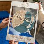 Two people holding a white framed personalized wooden first home map with layered Miami city design, heart location marker, and custom family text.