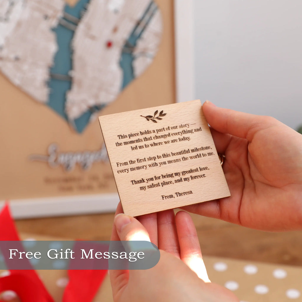 Hands holding a custom engraved wooden gift message card in front of a personalized heart map frame, showing the free gift message option for a meaningful engagement, anniversary, or wedding gift.