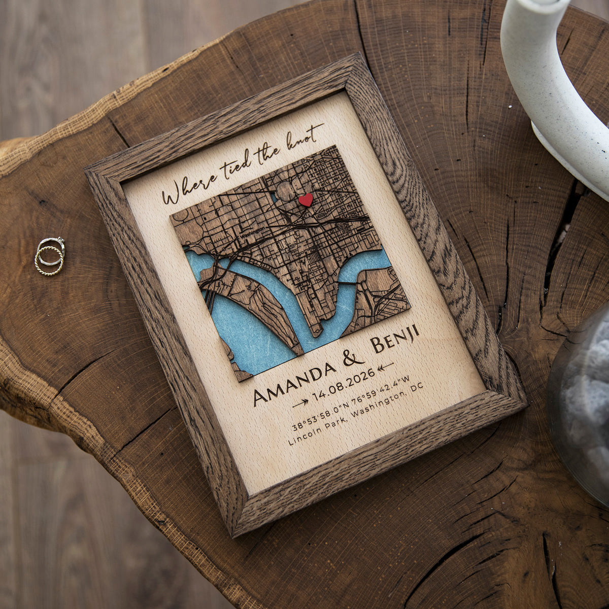 Handmade wooden wedding map held in hands with custom address, coordinates, couple names, and dark oak frame.