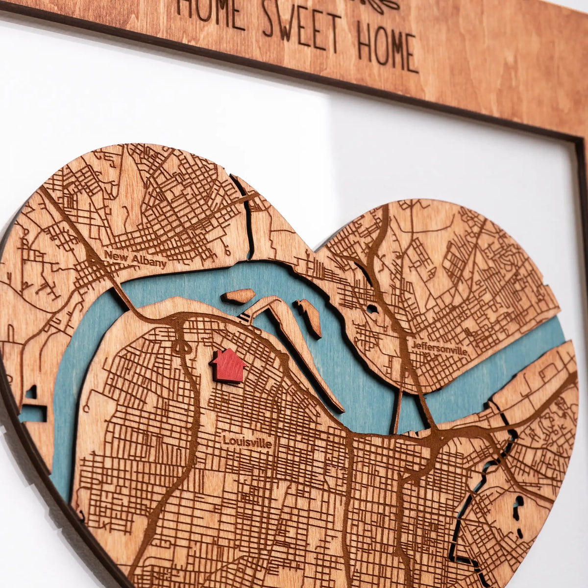 Close-up of heart-shaped personalized new home map with engraved city streets, blue river, and red home location pin