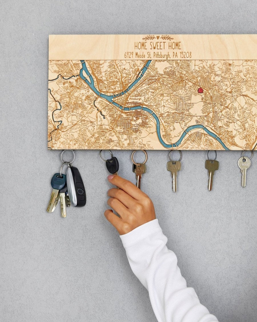 Key holder with map design on a gray wall, showing keys being hung.
