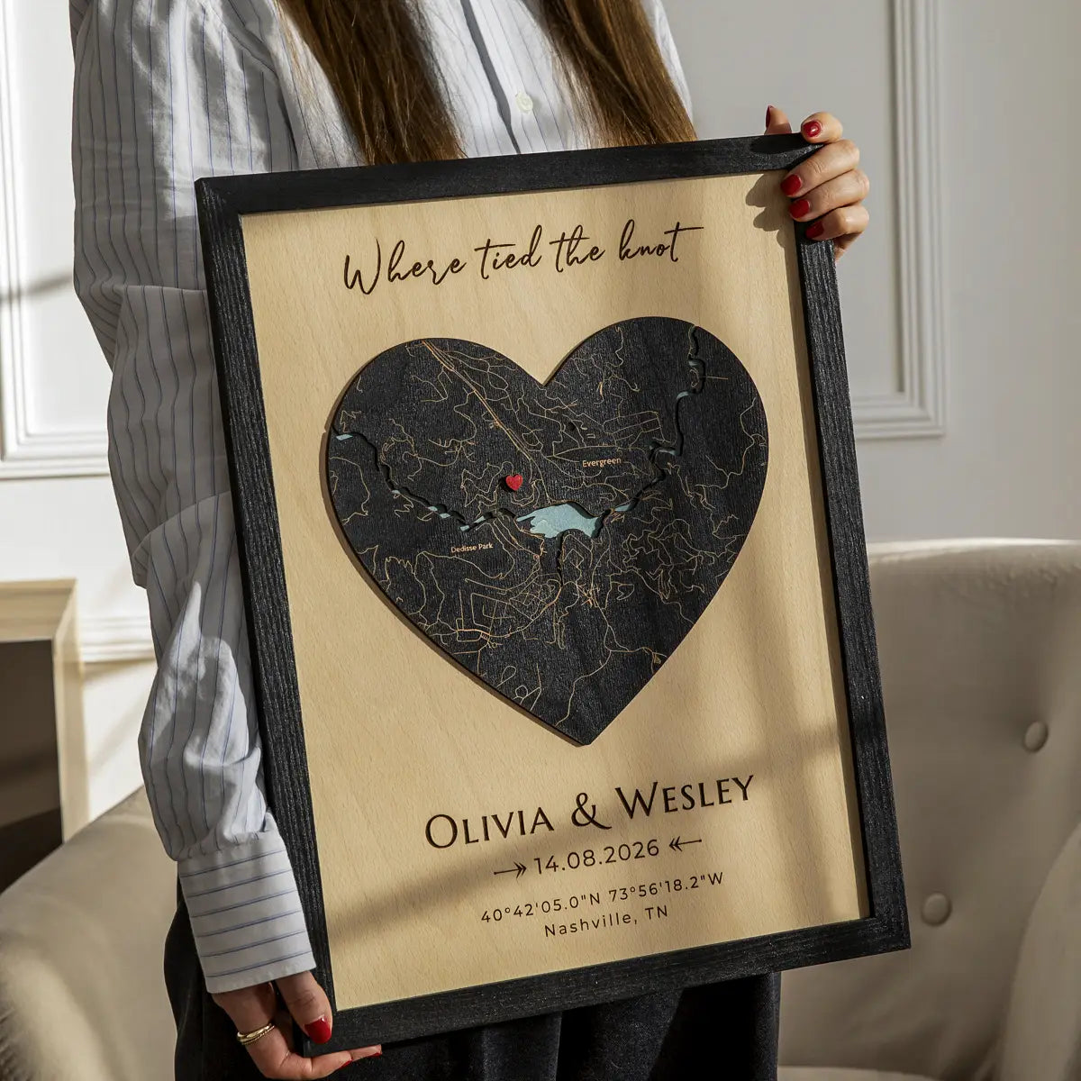 Person holding heart-shaped personalized wood map frame with “Where we tied the knot,” couple names, wedding date, and coordinates.