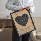 Person holding a framed heart-shaped map with location where it all began and personalized text in a room.