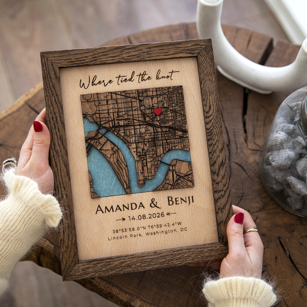 Wooden framed map with engraved text held by a person on a wooden surface.