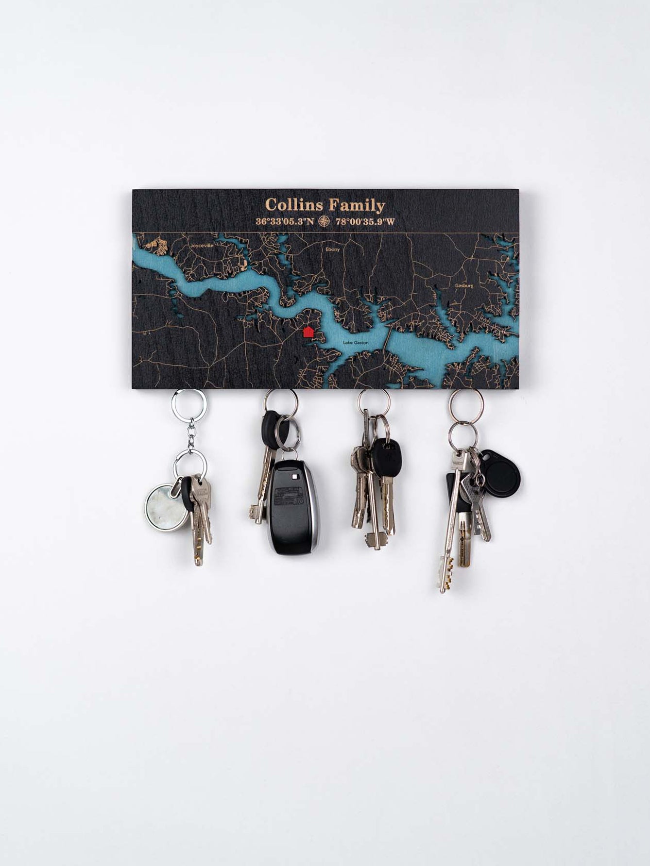 Key holder with a custom map design engraving text"and coordinates, mounted on a wall with multiple sets of keys hanging from magnetic.