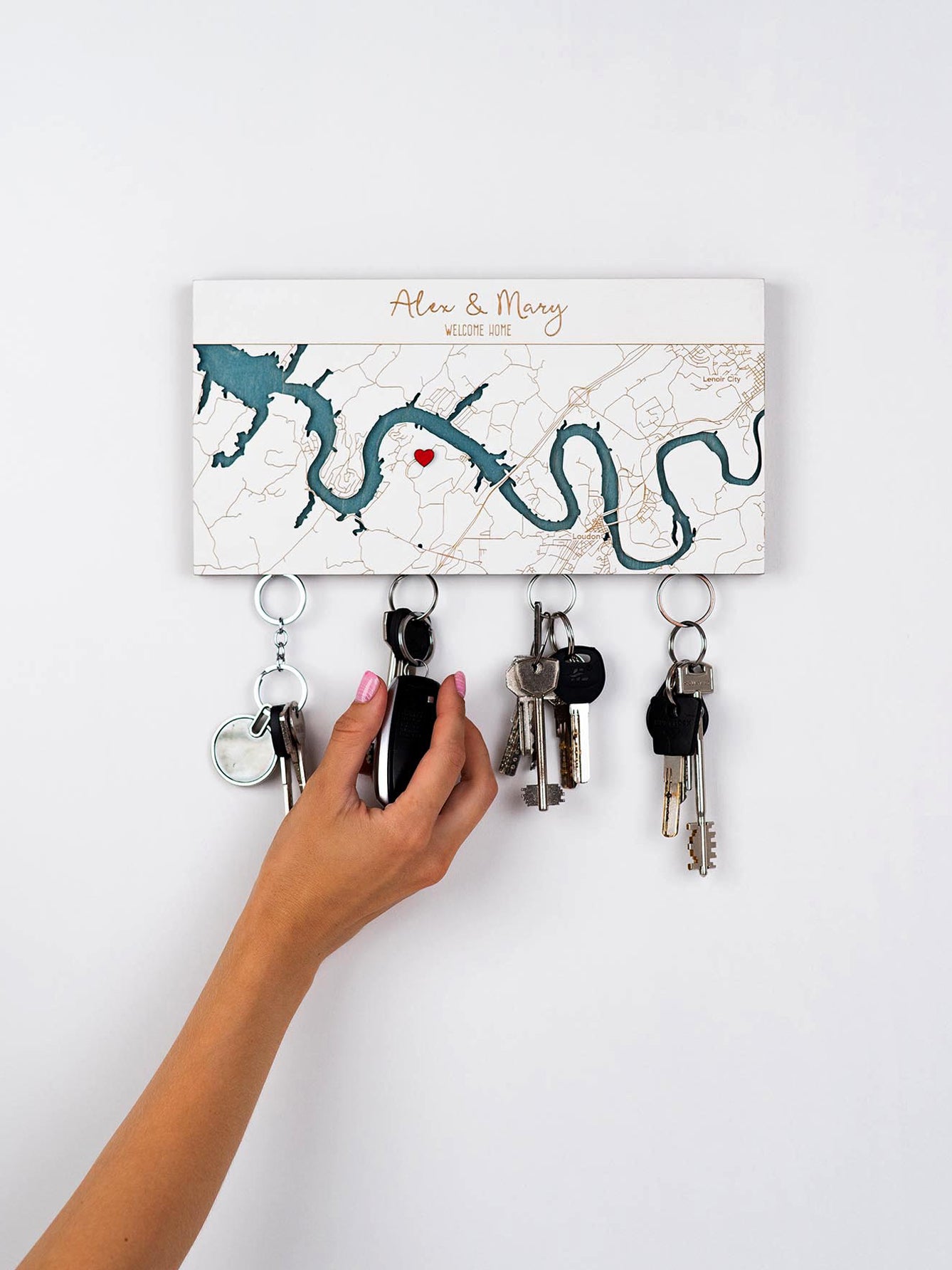 Person hanging keys on a decorative magnetic key holder with map design and the custom names and Welcome Home