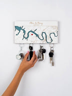 Person hanging keys on a decorative magnetic key holder with map design and the custom names and Welcome Home