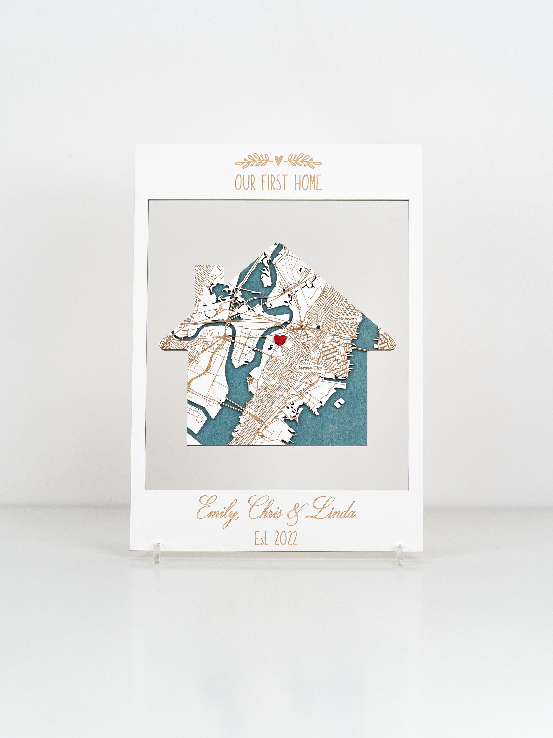 Customized housewarming gift with a cut-out map and a red heart marking, framed art reading "OUR FIRST HOME," personalized with names