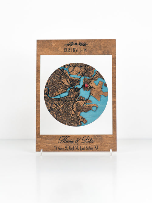 Custom wooden map art with text "OUR FIRST HOME" above a circle cutout featuring a detailed map personalized with names