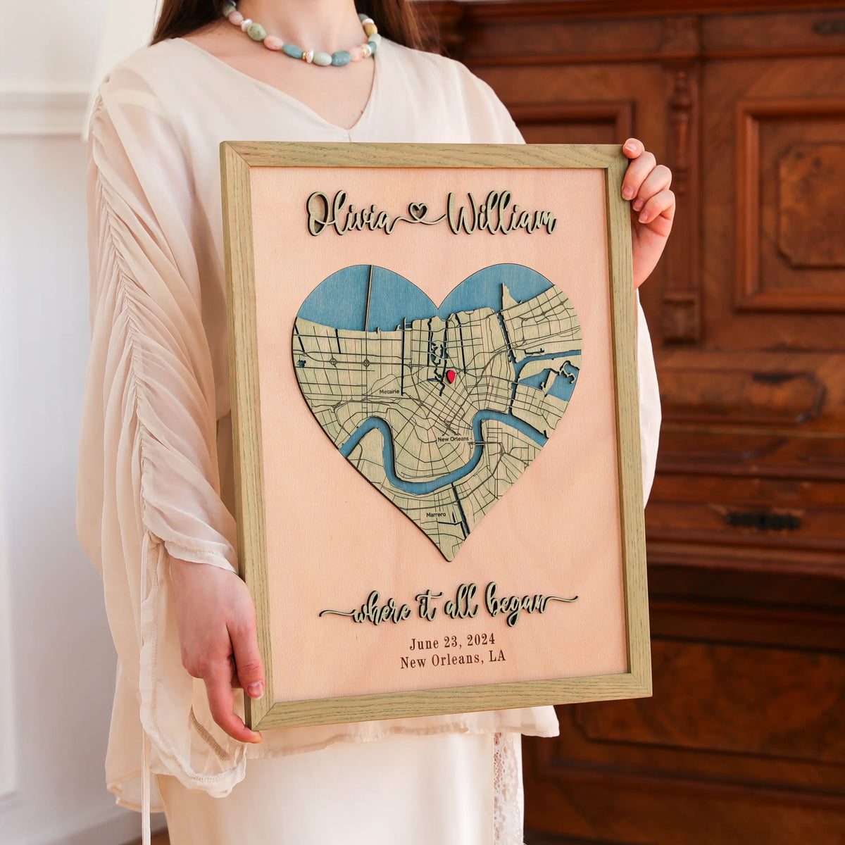 Woman holding a romantic personalized anniversary map for her with heart-shaped New Orleans location, raised 3D names, custom date, and sage oak frame.
