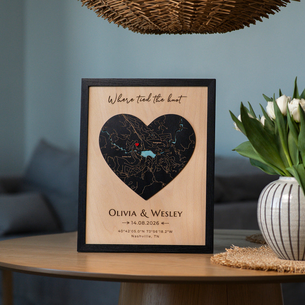 Personalized wooden wedding map being placed on the wall with black frame, heart-shaped map, red pin, and couple details.