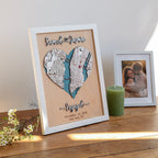 Personalized wedding anniversary gift with heart-shaped New York location map, raised names, engagement wording, white frame, candle, flowers, and couple photo in the background.