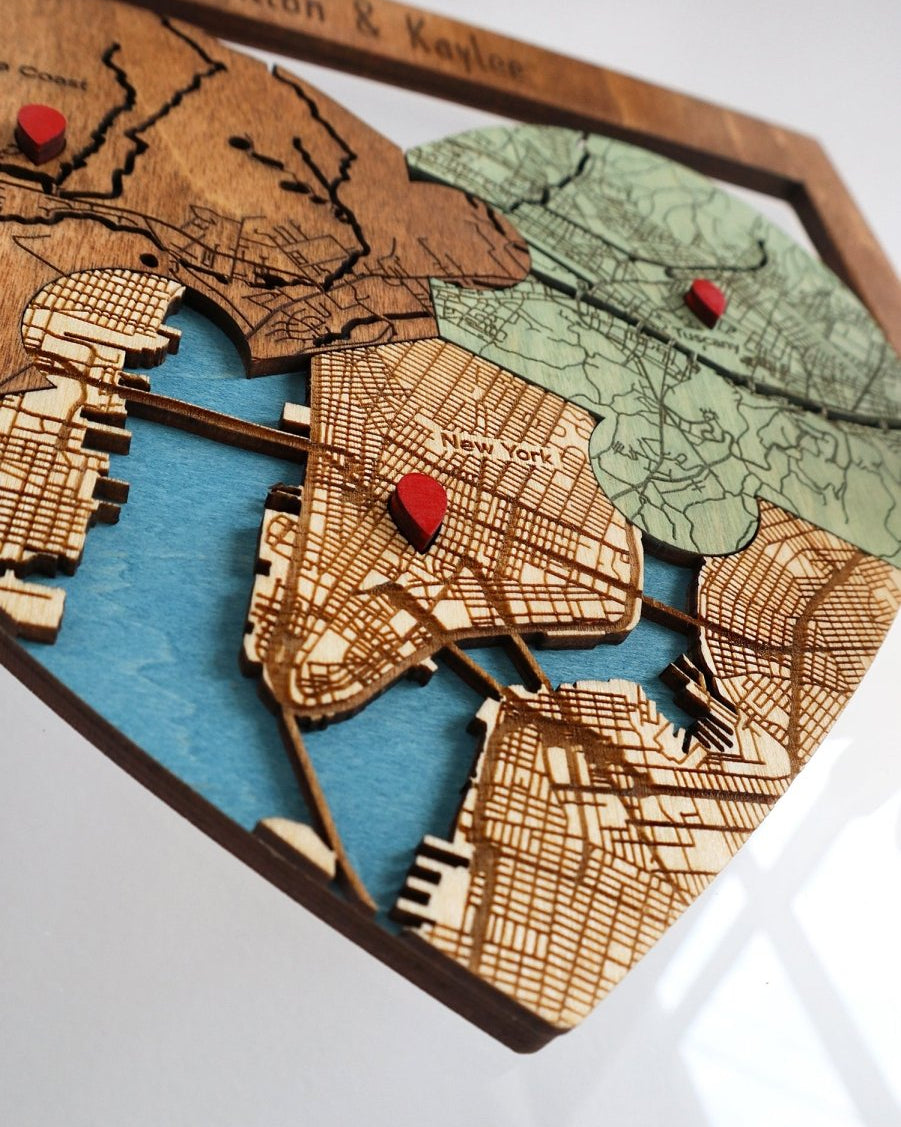 Wooden map cutout with engraved details and red pins on a white background