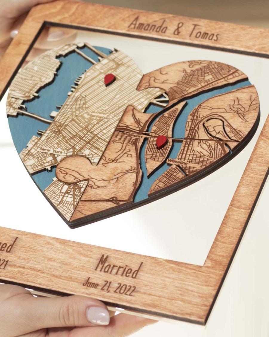 Wooden heart-shaped cutout with engraved map design and personalized text, held by a hand.
