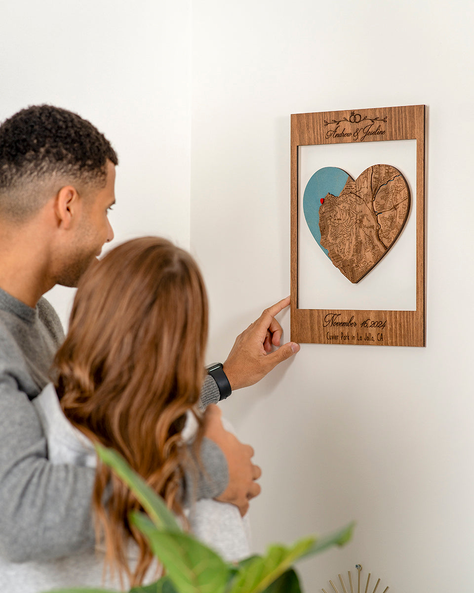Man and woman looking at a wooden heart-shaped map framed picture on a wall.