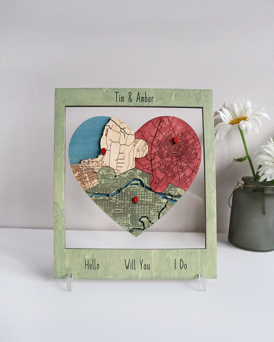 Heart-shaped map collage with 'Tim & Amber' text, 'Hello Vill You I Do' message, and a vase of flowers on a white background.