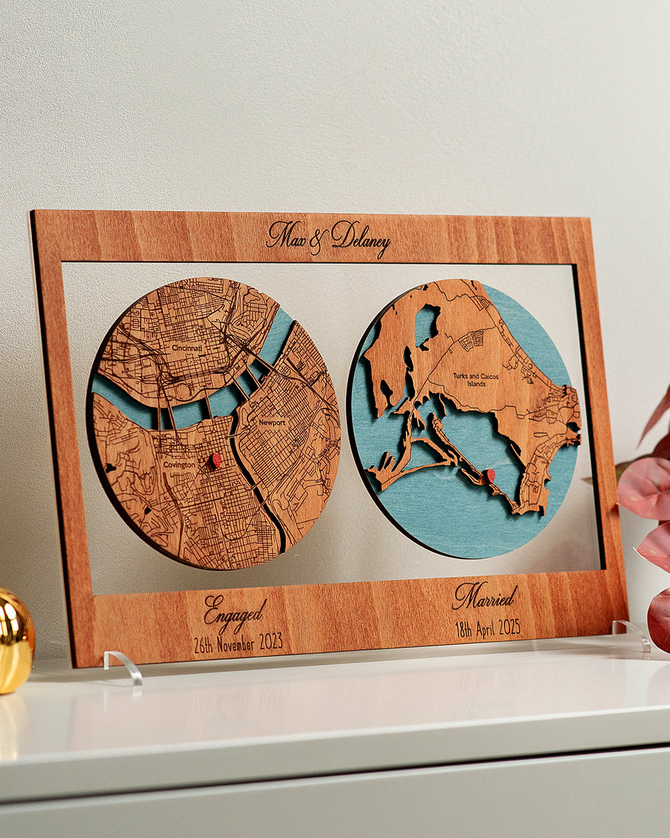 Wooden framed map of two locations with engraved dates, held by a hand.
